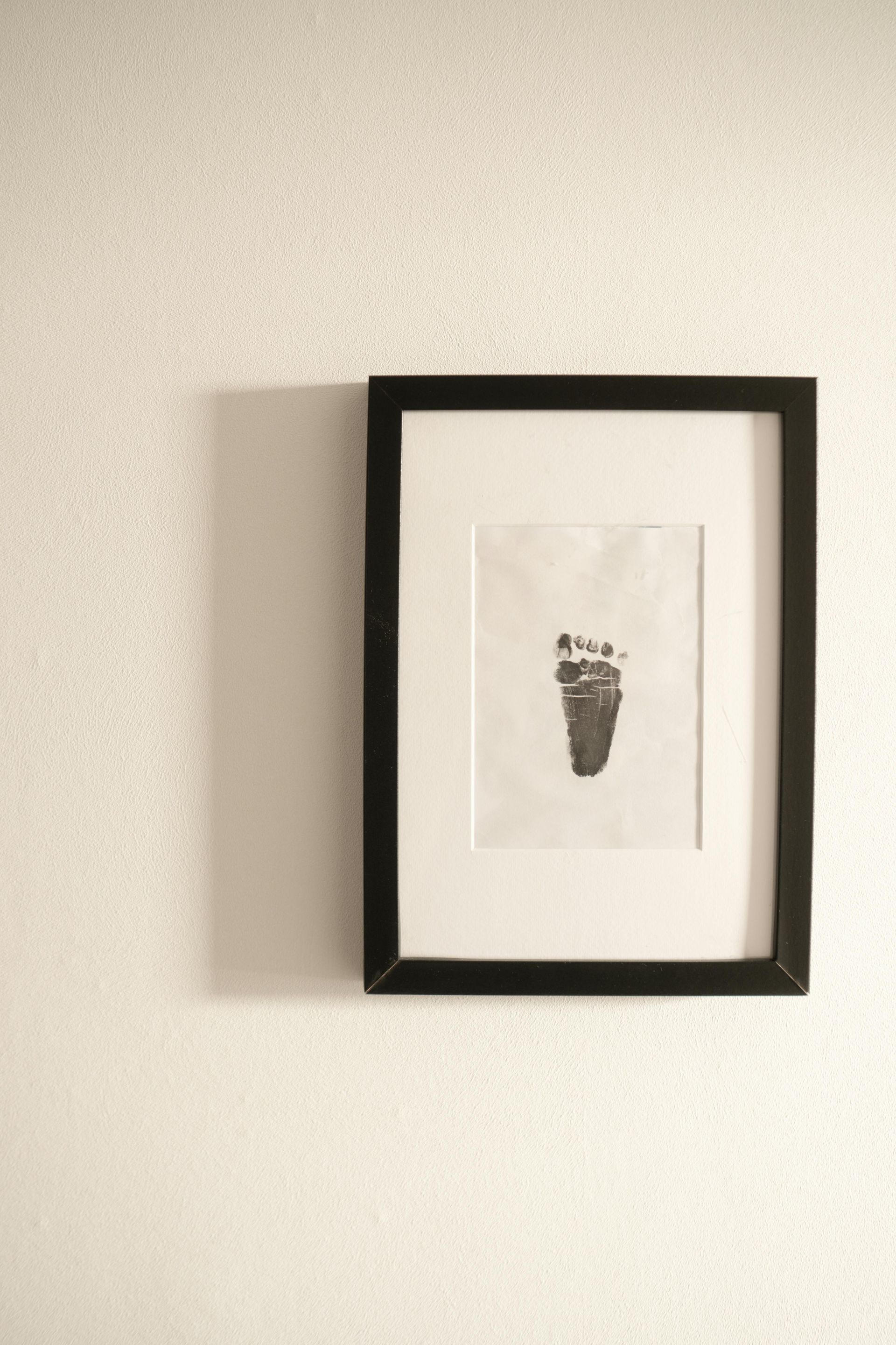 Framed minimalist print with a tiny dark footprint on a white wall