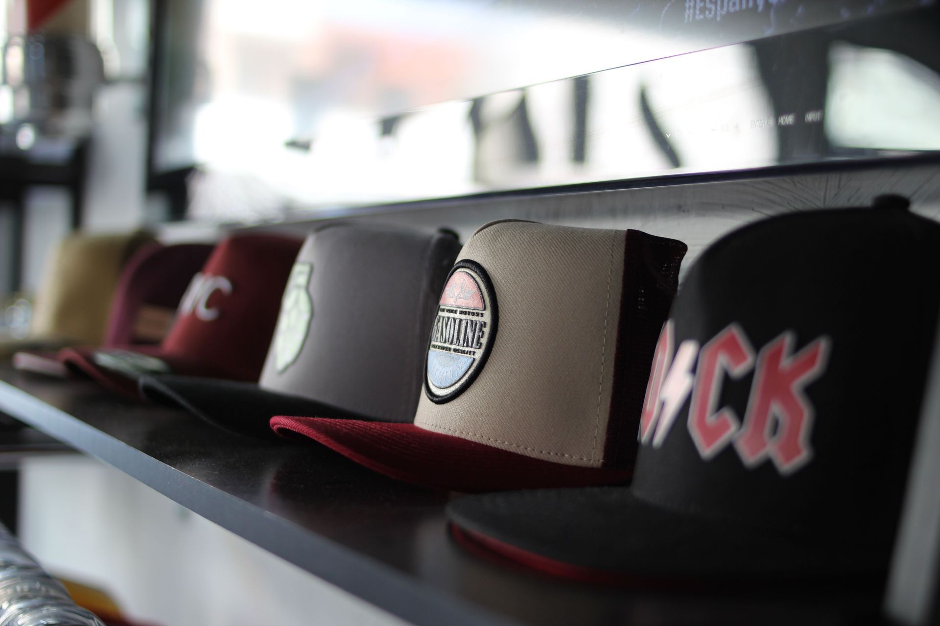 Row of baseball caps displayed on a store shelf, including black, red, and tan hats with logos