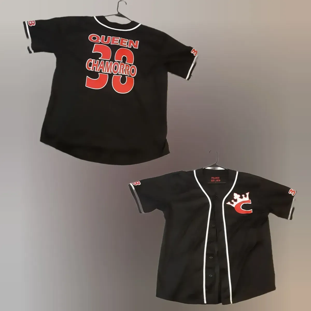 Two black Cincinnati Reds shirts displayed on hangers, one front and one back, with red and white graphics.