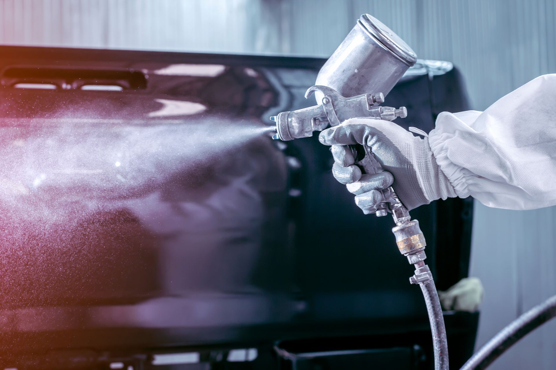 Person in protective suit using spray gun to paint a car panel.
