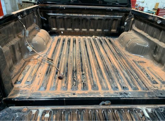 Black truck bed with reddish-brown dirt and longitudinal grooves.