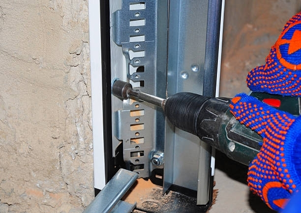 A person is using a drill to fix a garage door.