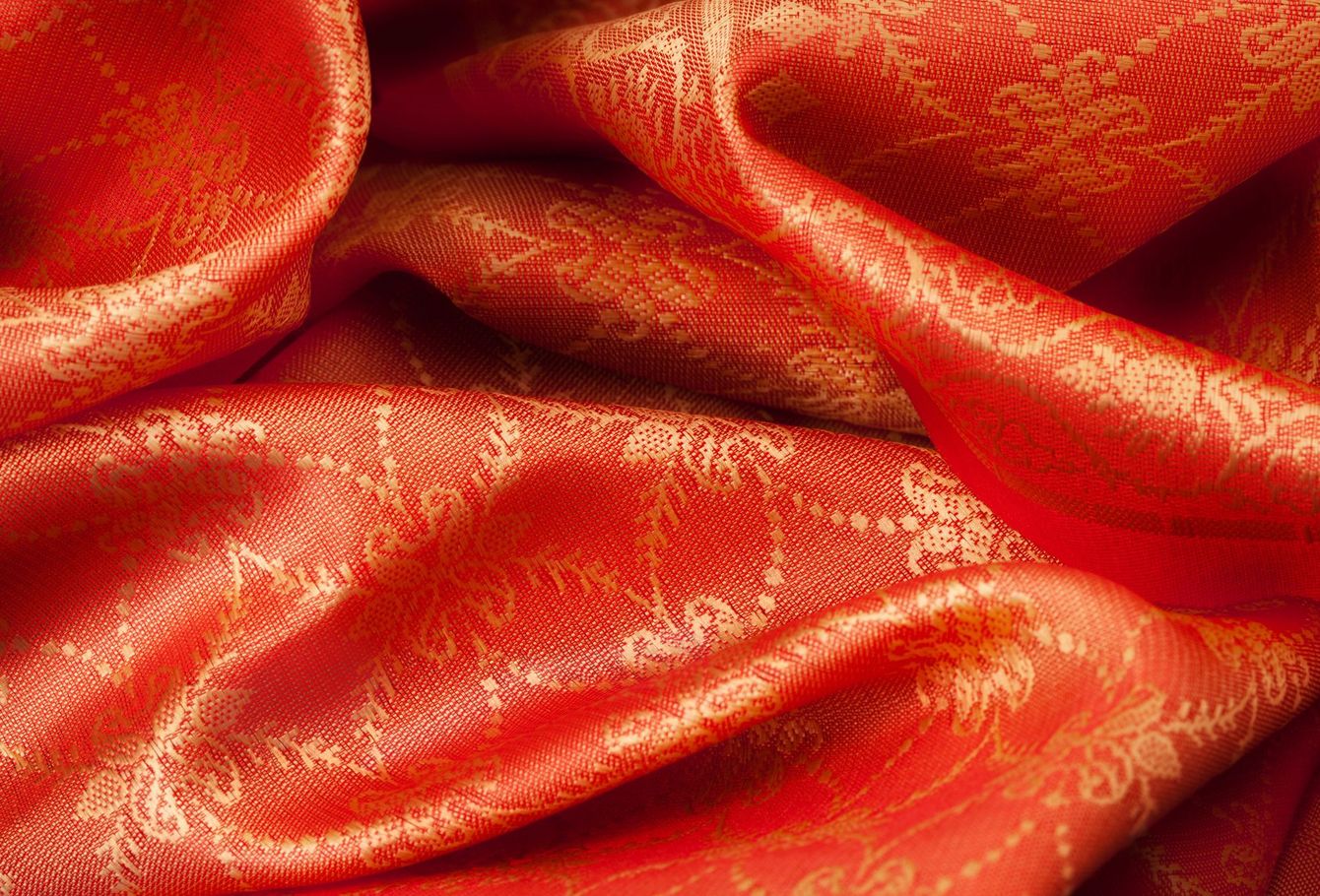 Primer plano de una tela de seda rojo anaranjada brillante con intrincados estampados florales dorados.