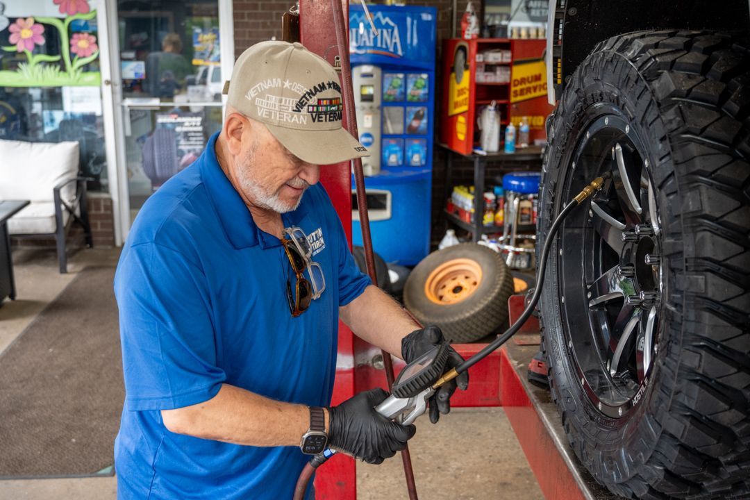 Mechanic polishing a large black tire with a buffer in an auto shop
