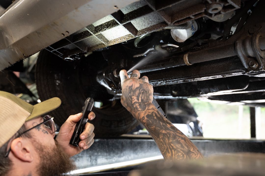 Mechanic inspecting the underside of a vehicle with a flashlight and phone in a garage