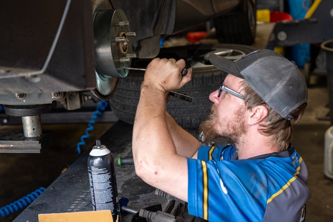 Mechanic in blue shirt and cap working under a vehicle with a tool in a garage