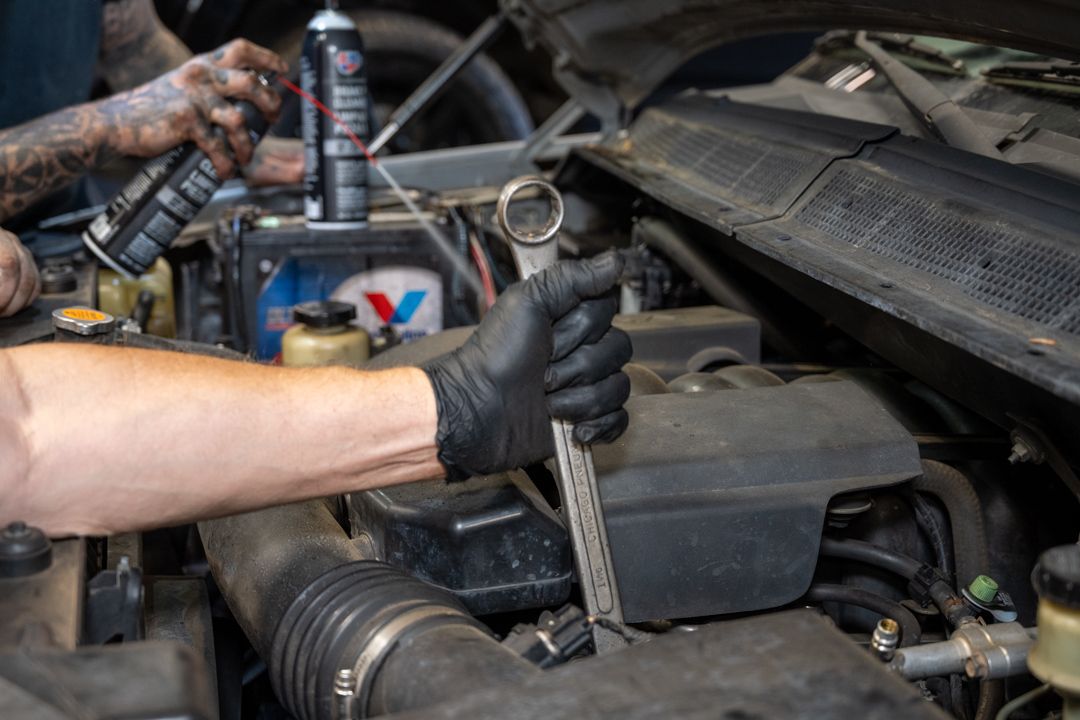 Gloved hands using a wrench to tighten a car engine bolt in an open hood bay