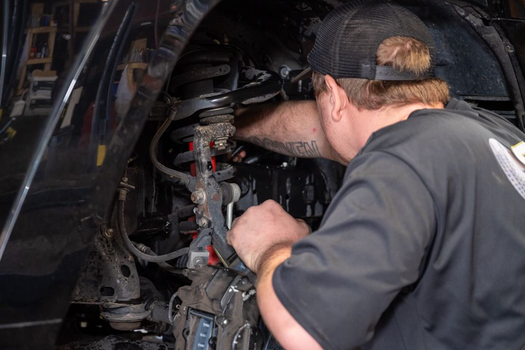 Mechanic working inside a vehicle engine compartment with tools, focused on repairs