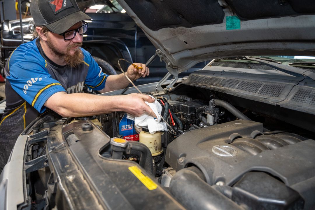 Mechanic in a blue shirt works under an open car hood in a garage