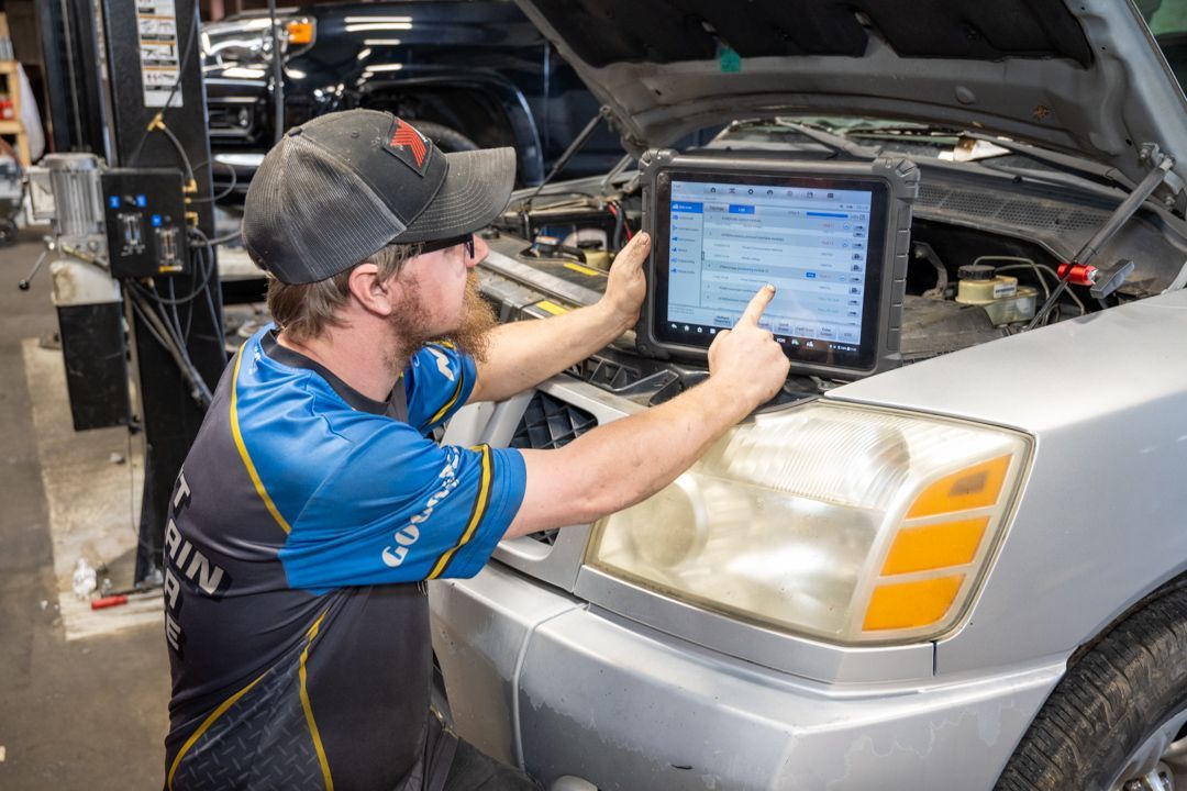 Mechanic using a tablet to diagnose a silver car in an auto repair shop