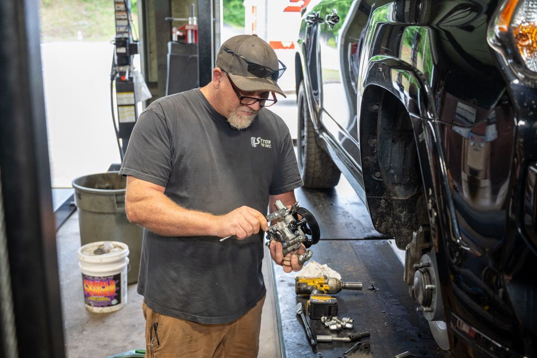 Mechanic polishing a black vehicle in a garage, holding a power buffer beside tools and cleaning supplies