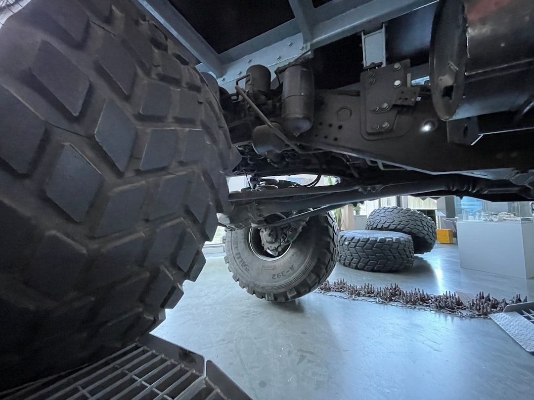 Low-angle view under a lifted off-road truck, showing large tires and snowy ground beneath.