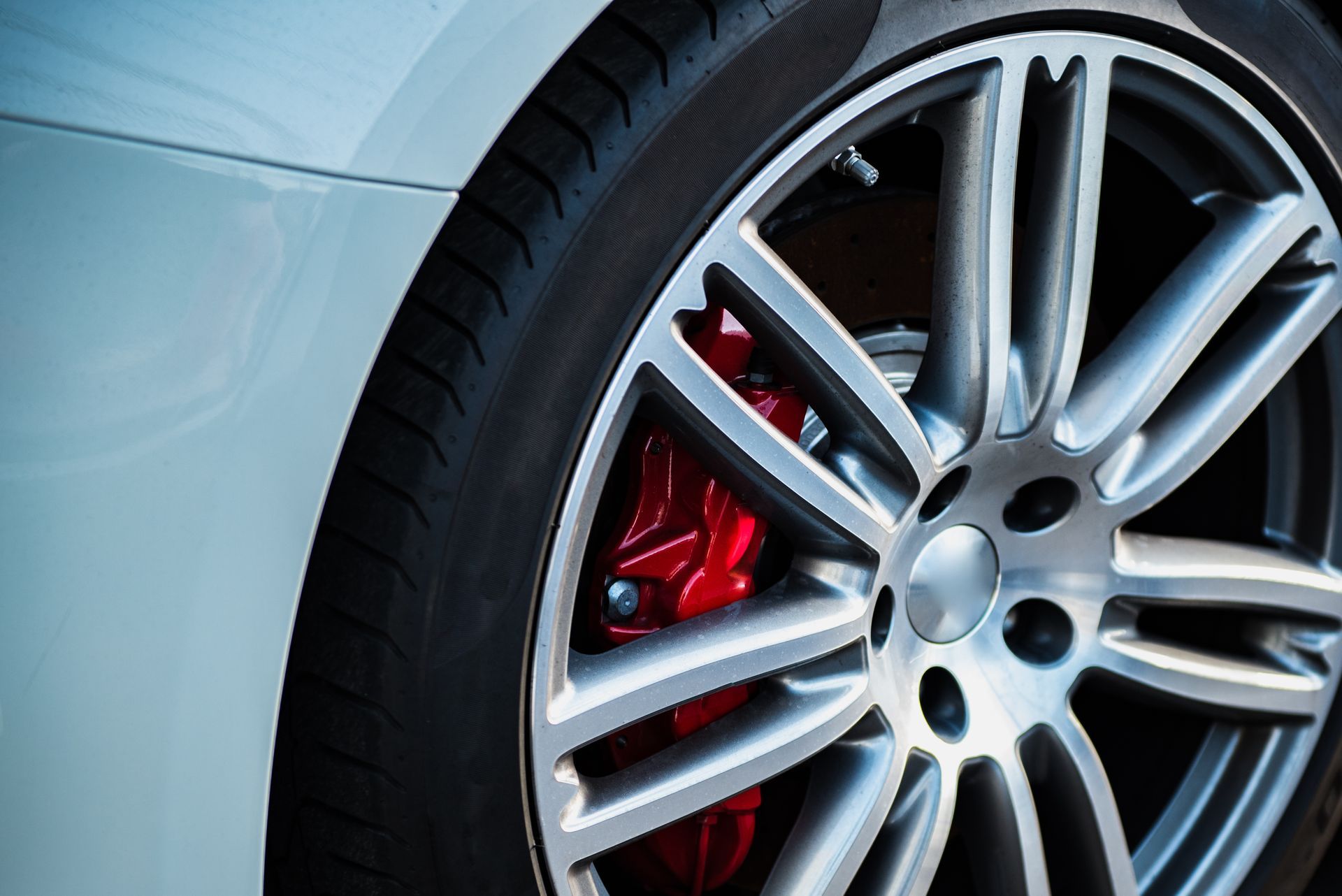 Close-up of a silver car wheel with red brake caliper and white body panel