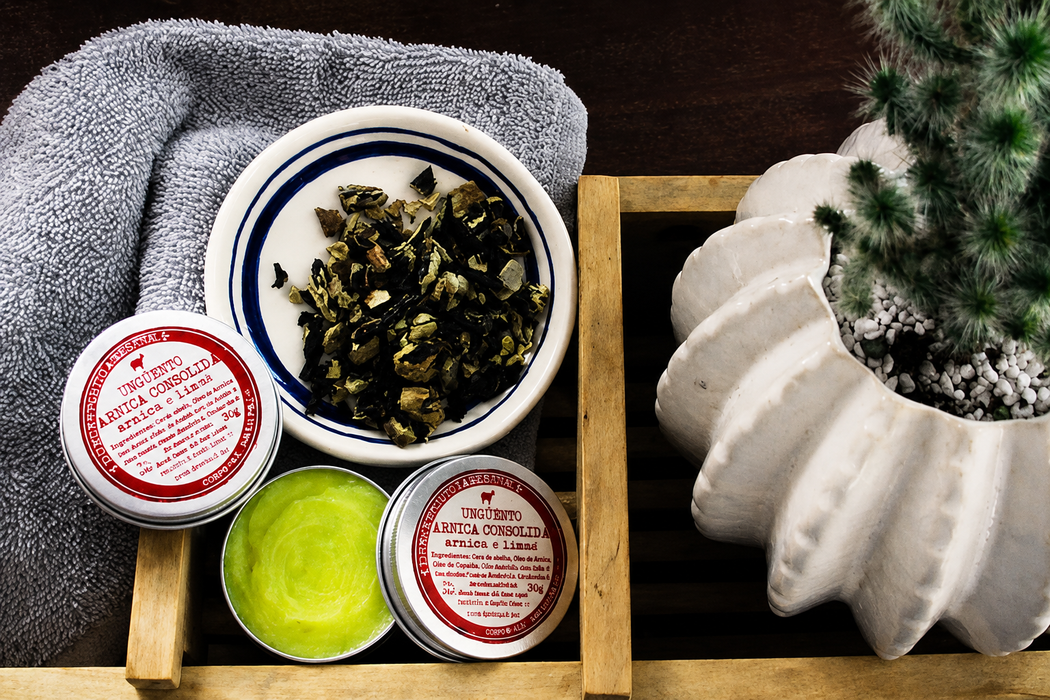 Vassoio da spa con asciugamani, vasetti di prodotti per la cura della pelle, una crema verde e una piccola pianta in vaso su una superficie di legno.
