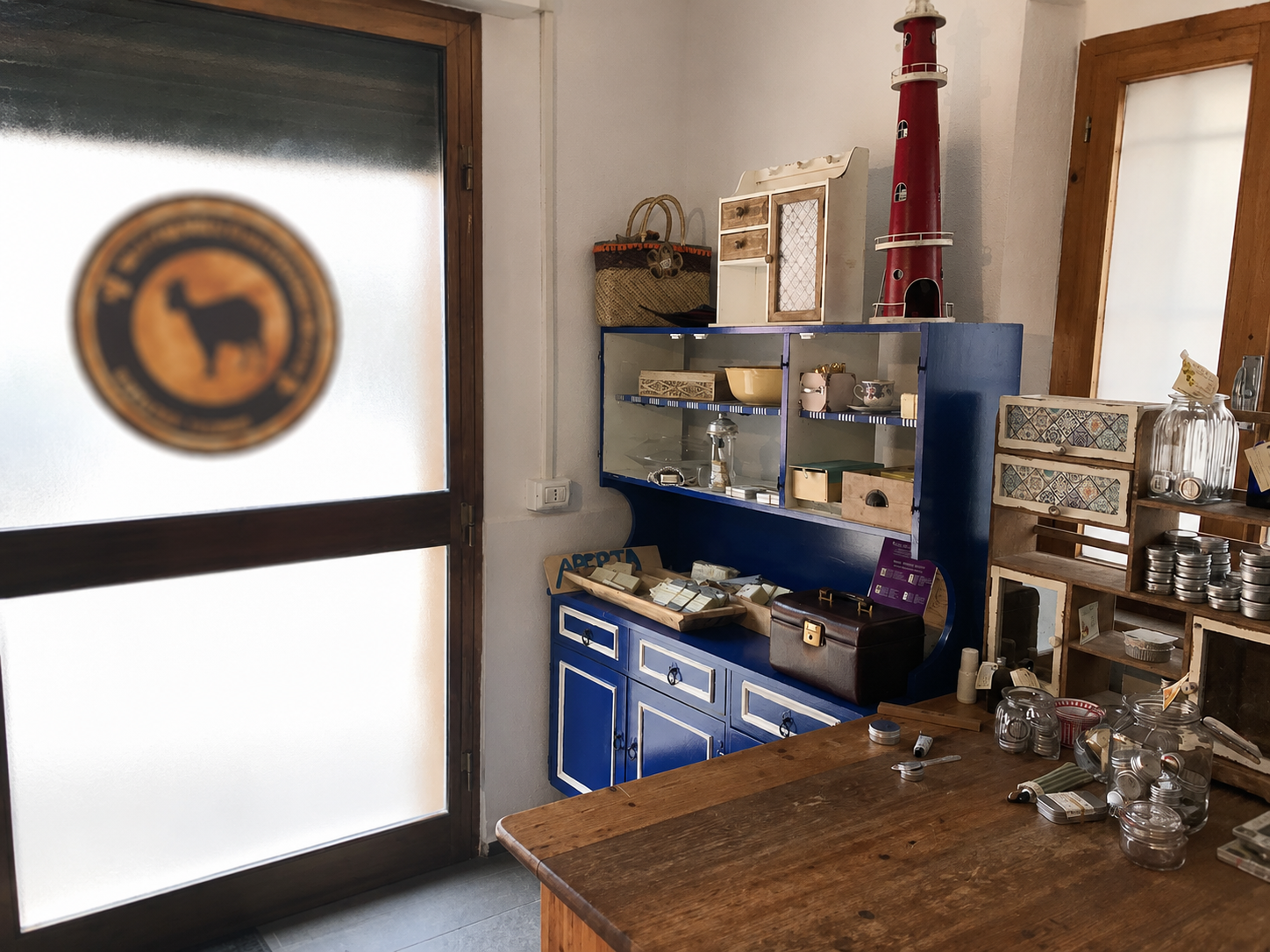 Piccolo bancone con tavolo in legno, scaffali blu e porta satinata con logo circolare.