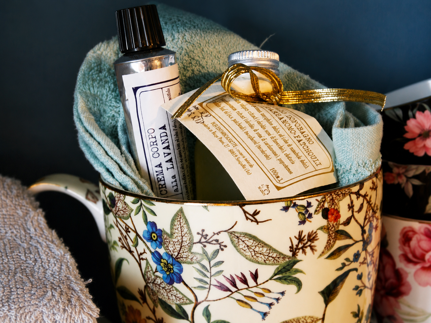 Cesto regalo con bottiglia, tessuto piegato e cartellino, decorato con carta da regalo floreale e nastro.