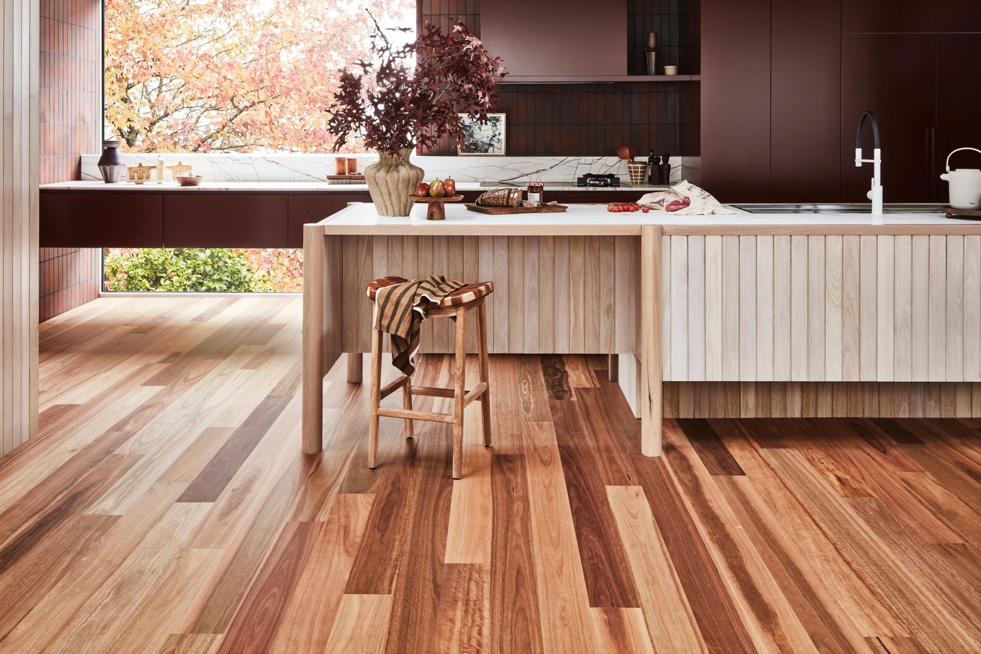 Kitchen with wood floors and island. Burgundy cabinetry, light wood island, and window with fall foliage.