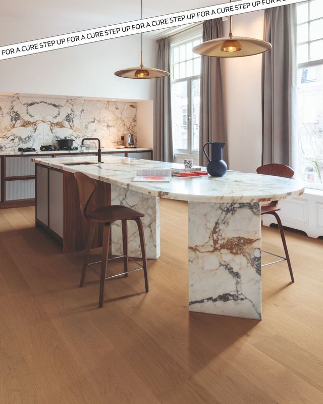 A modern kitchen with a marble island and backsplash, wooden floor, and pendant lights.