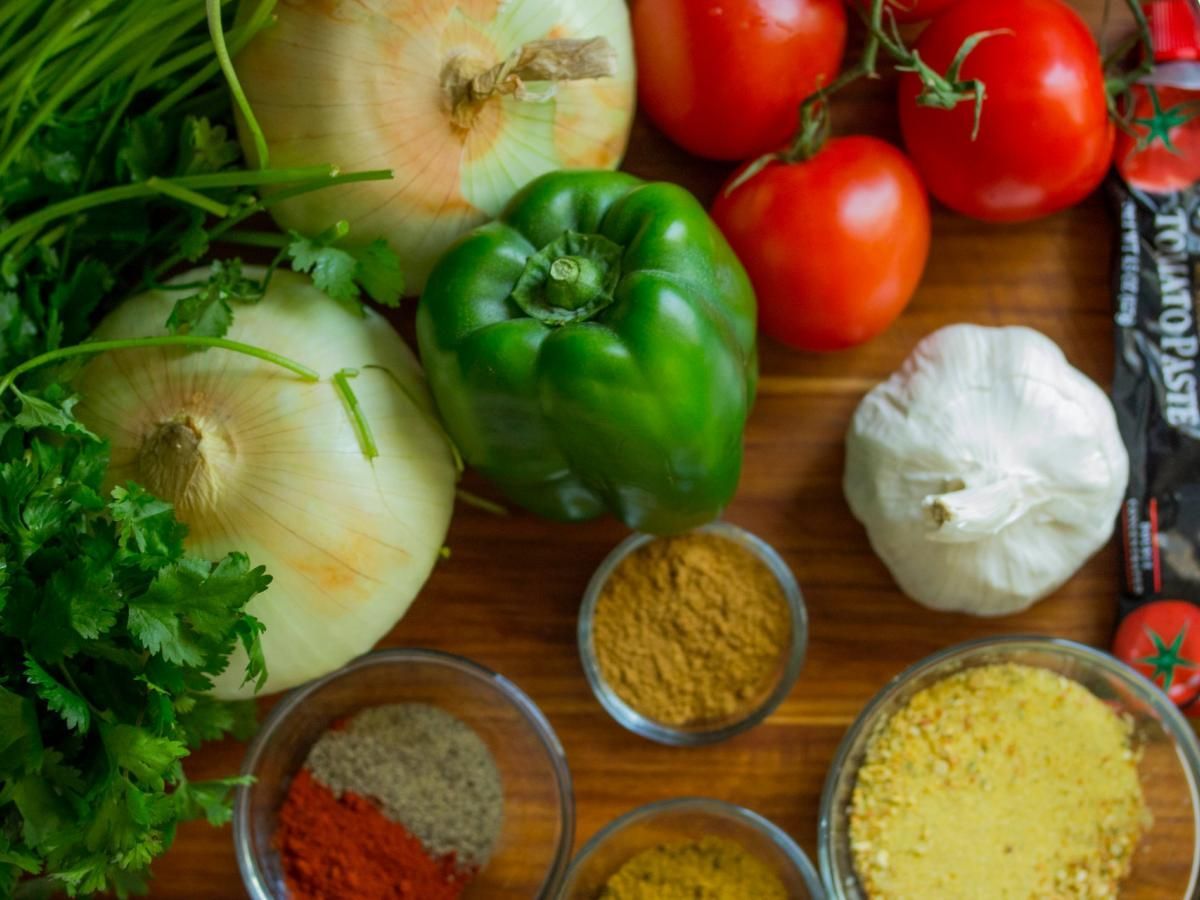 A variety of vegetables and spices are on a wooden table.