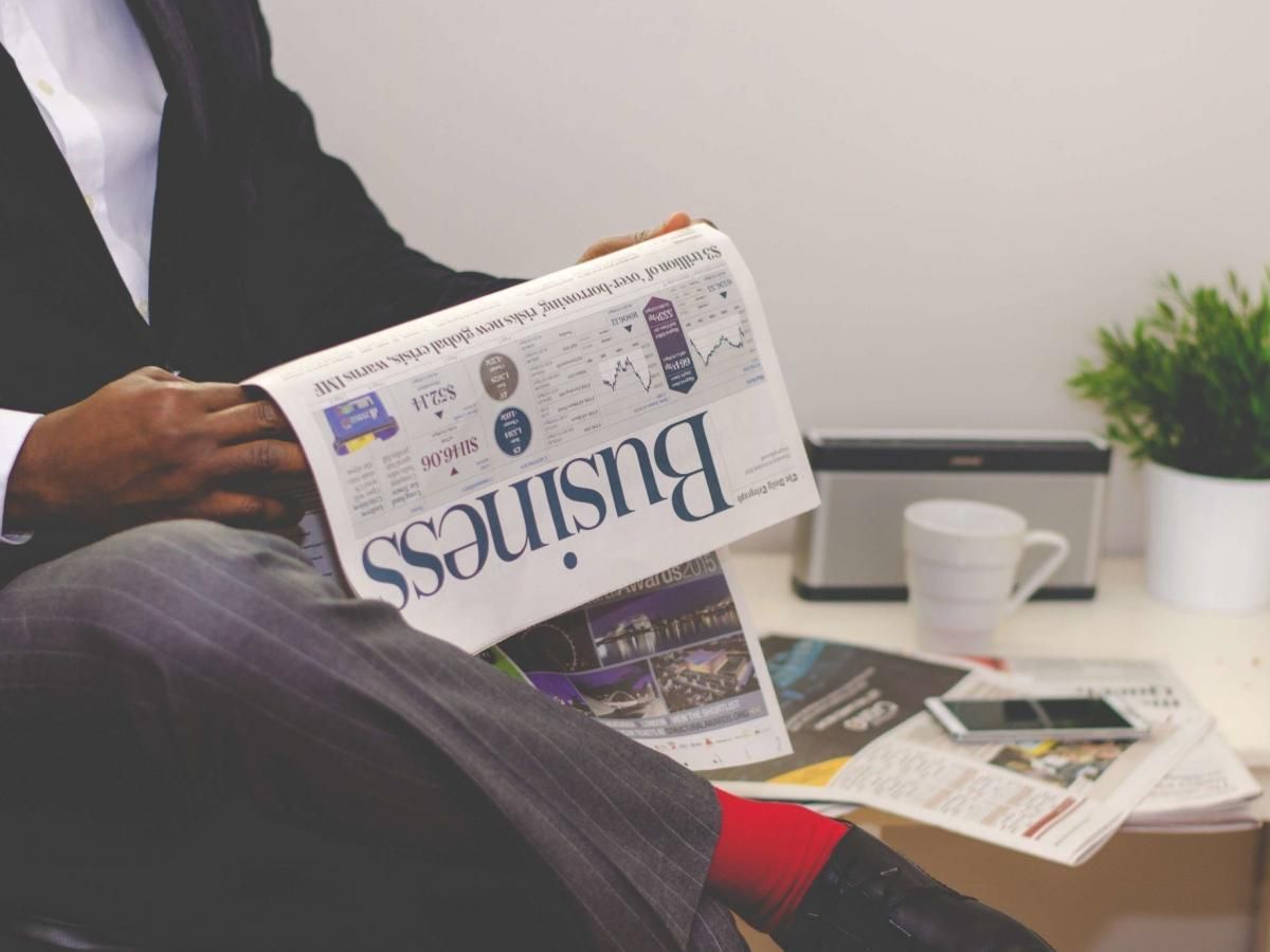 A man is sitting at a table reading a business newspaper.