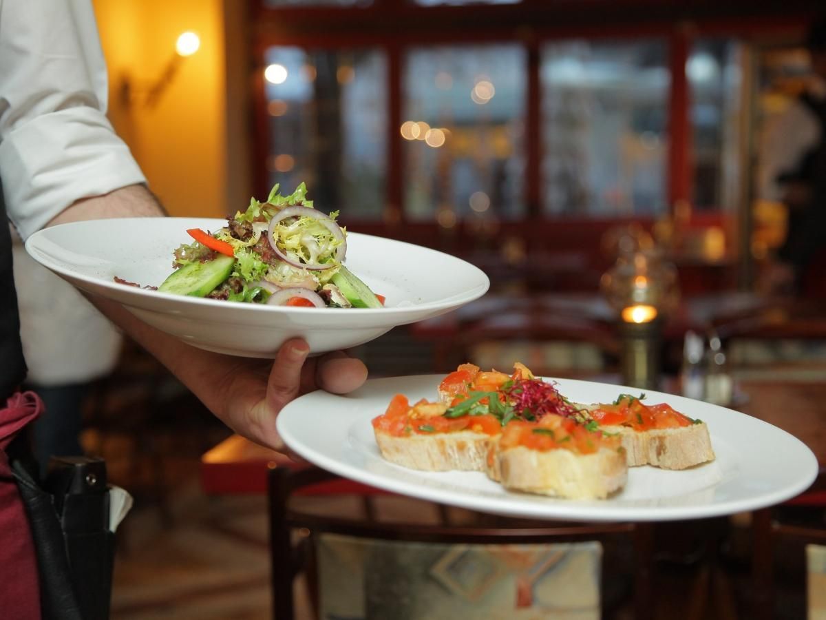 A waiter is carrying two plates of food in a restaurant.