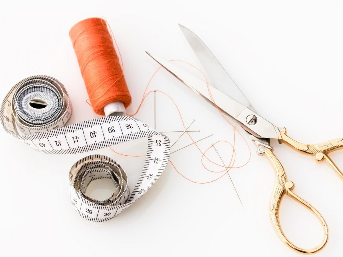 A pair of scissors measuring tape and a spool of thread