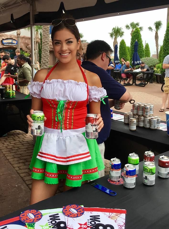 A woman in a red white and green dress is holding two cans of beer