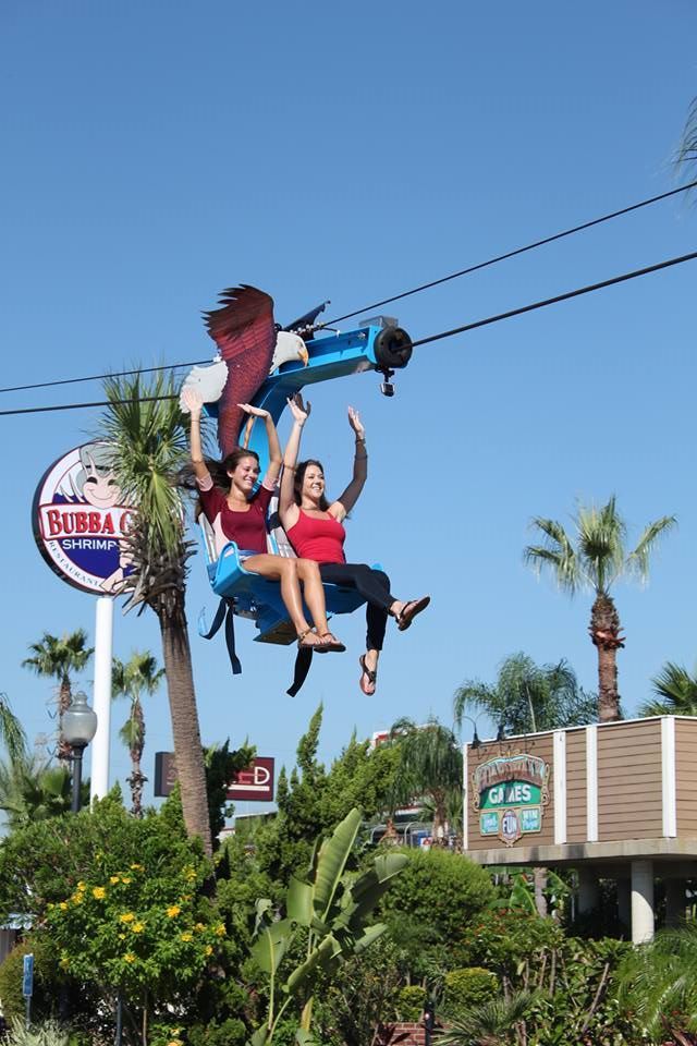 Two people are riding a zip line in front of a bubba gump sign