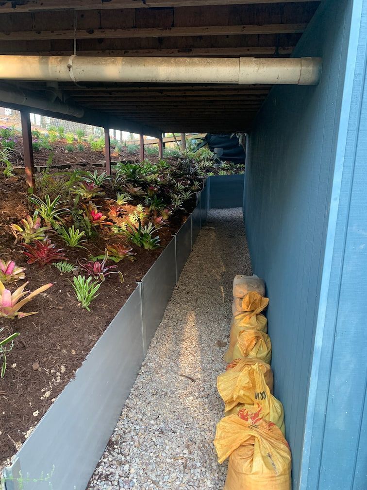 A walkway under a house with bags of dirt and plants.