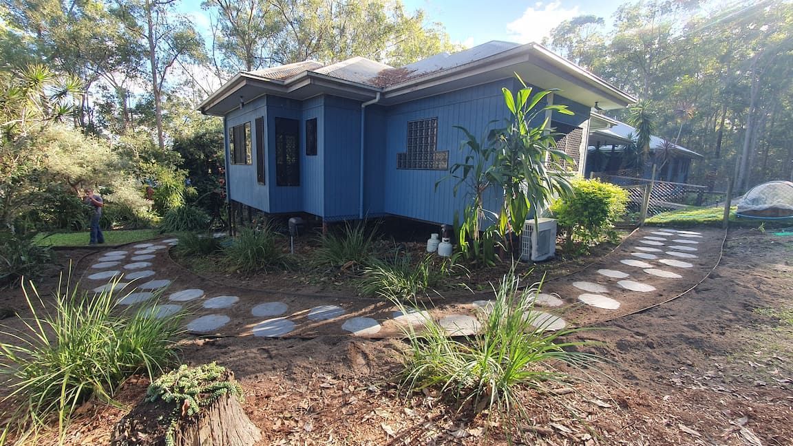 A small blue house with a stone walkway leading to it is surrounded by trees.