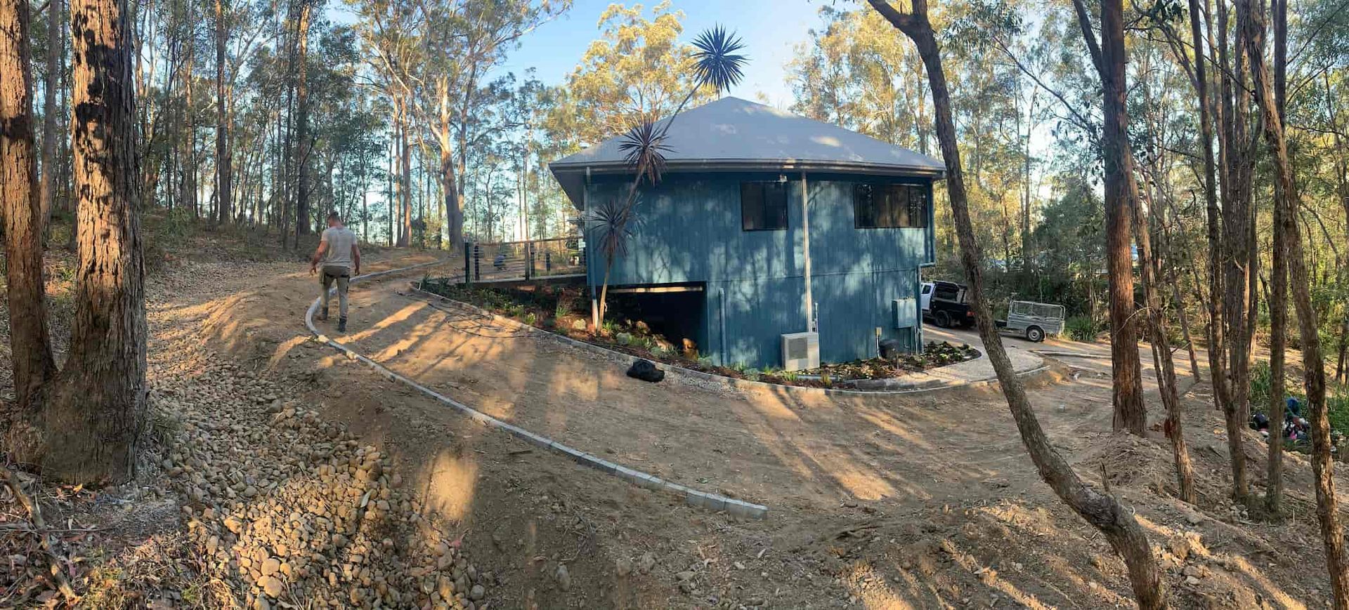 A blue house is sitting on top of a dirt hill in the middle of a forest.