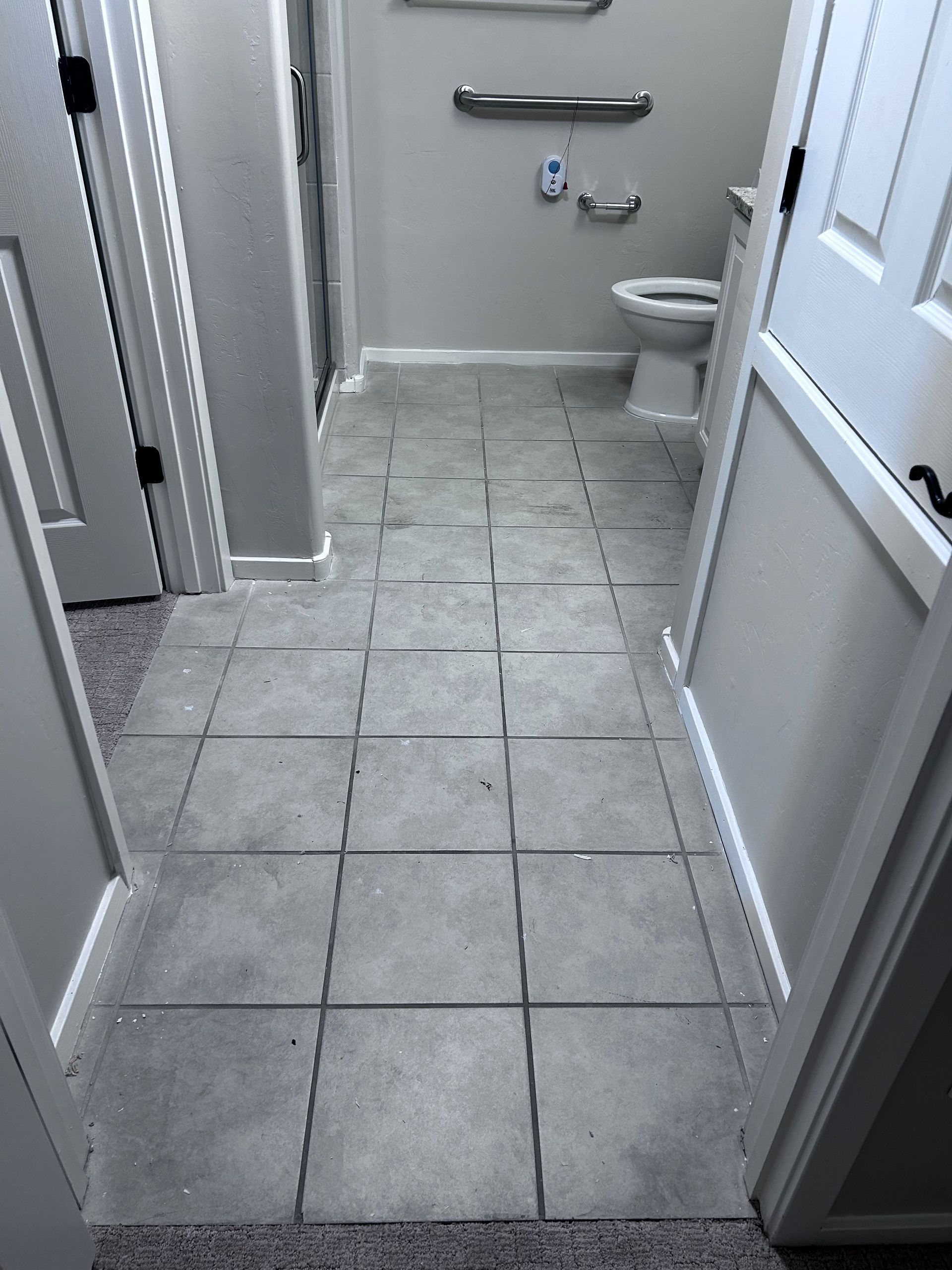 Narrow tiled hallway leading to a bathroom with a toilet and wall-mounted grab bars.