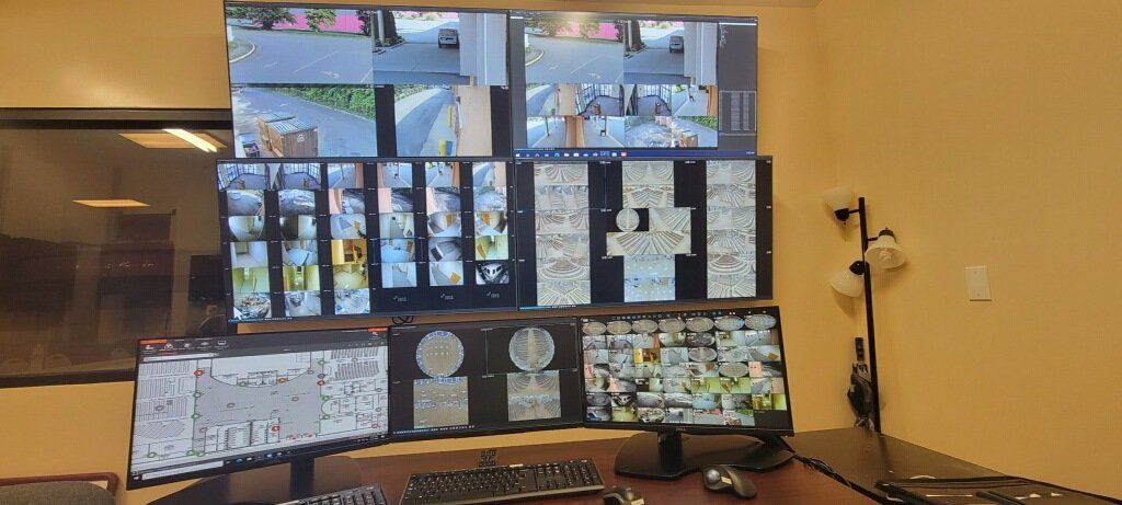 A security control room with multiple monitors displaying surveillance camera feeds.