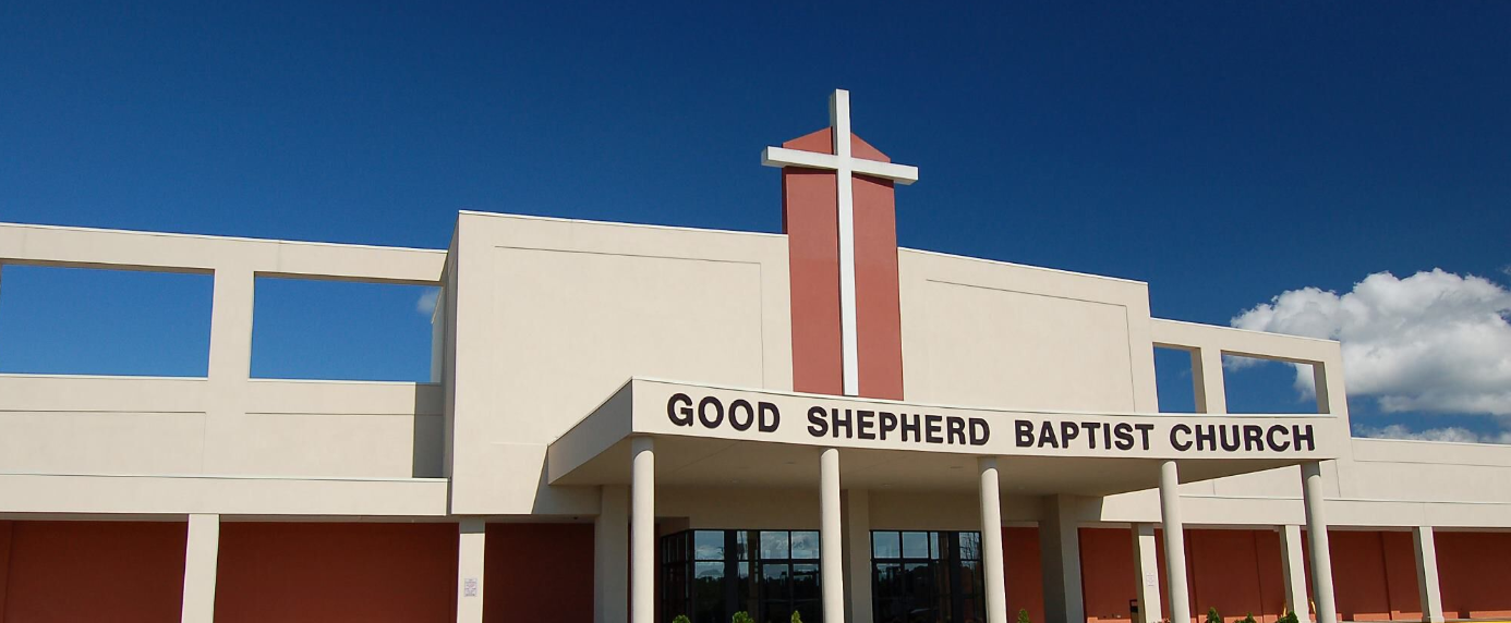 Good Shepherd Baptist Church with a cross on top, against a blue sky.