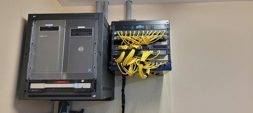 Server rack with two computers, a switch, and yellow network cables mounted on a wall.