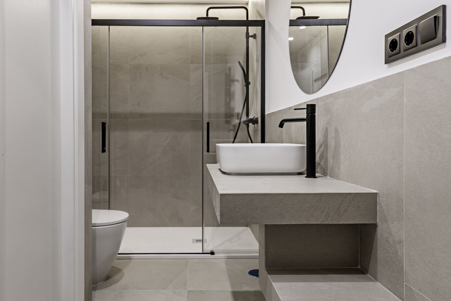 A modern bathroom with grey tiling, a shower cabin with a glass screen and black taps.