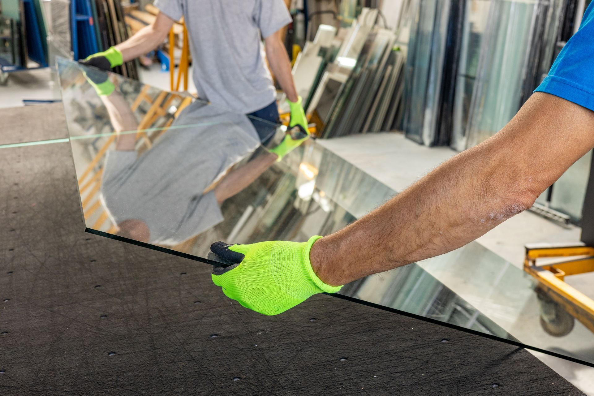Two glaziers holding a large sheet of thick glass by hand.