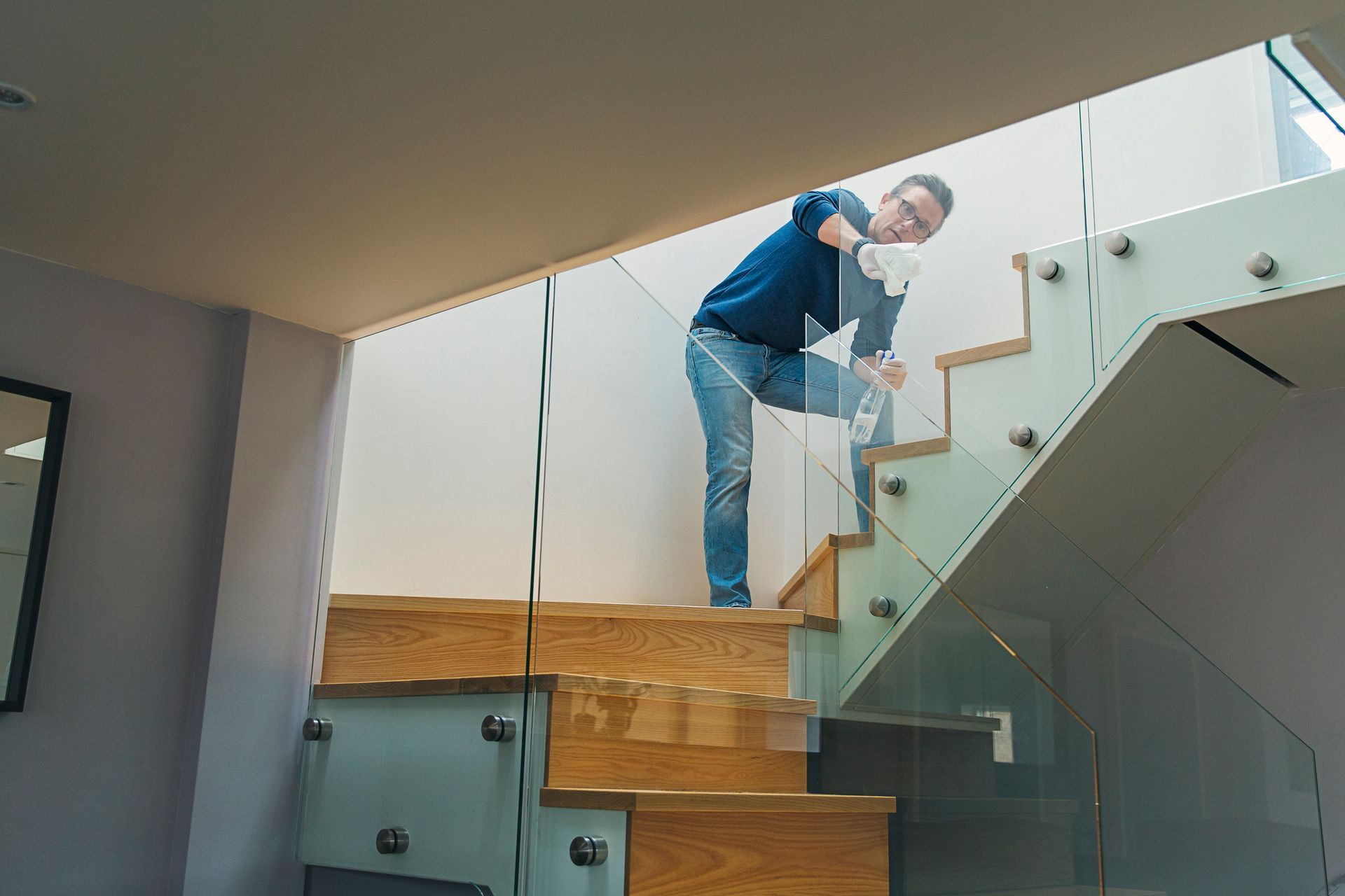 Person cleaning a glass balustrade on a wooden staircase with metal brackets.