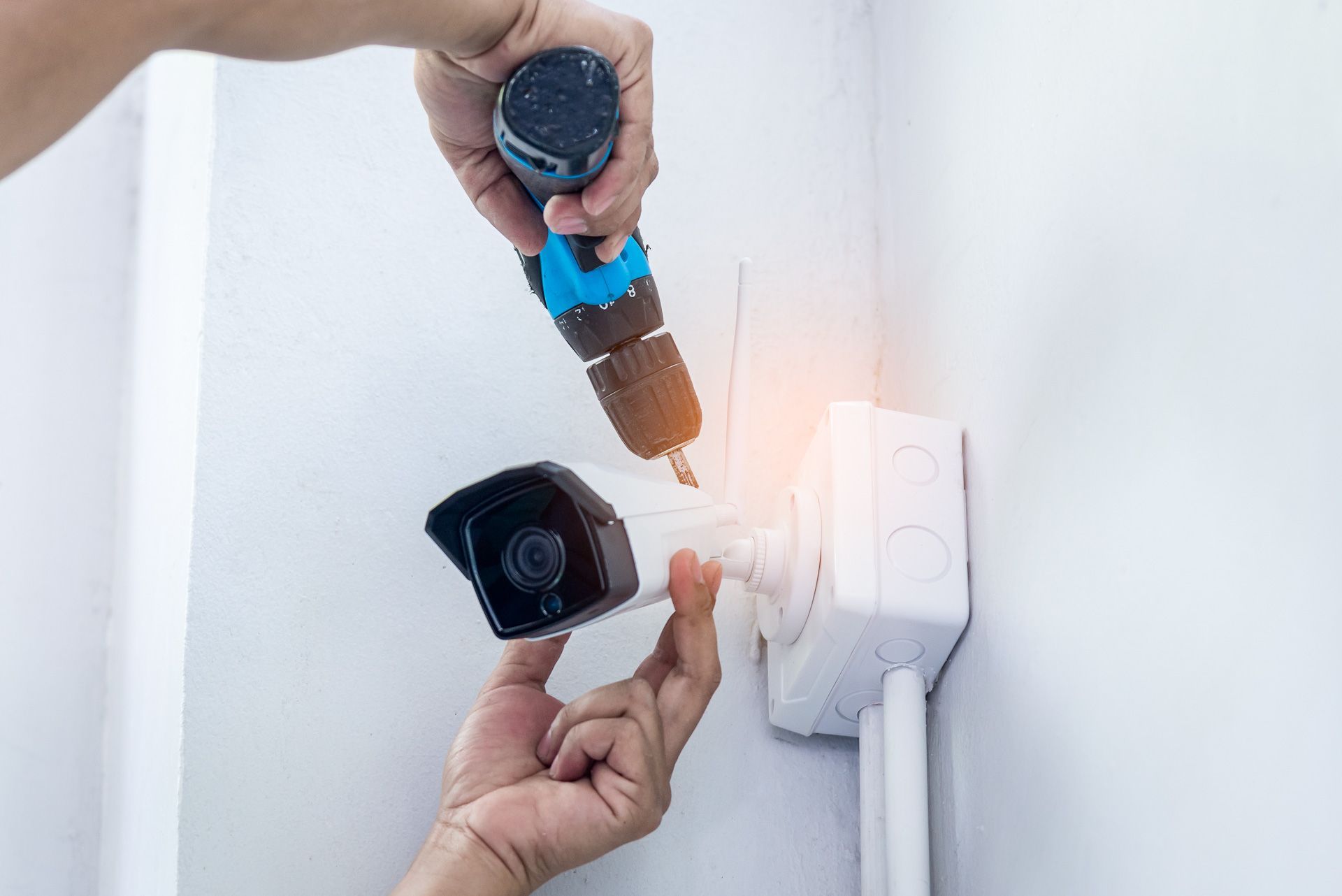 A person is installing a security camera on a wall with a drill.