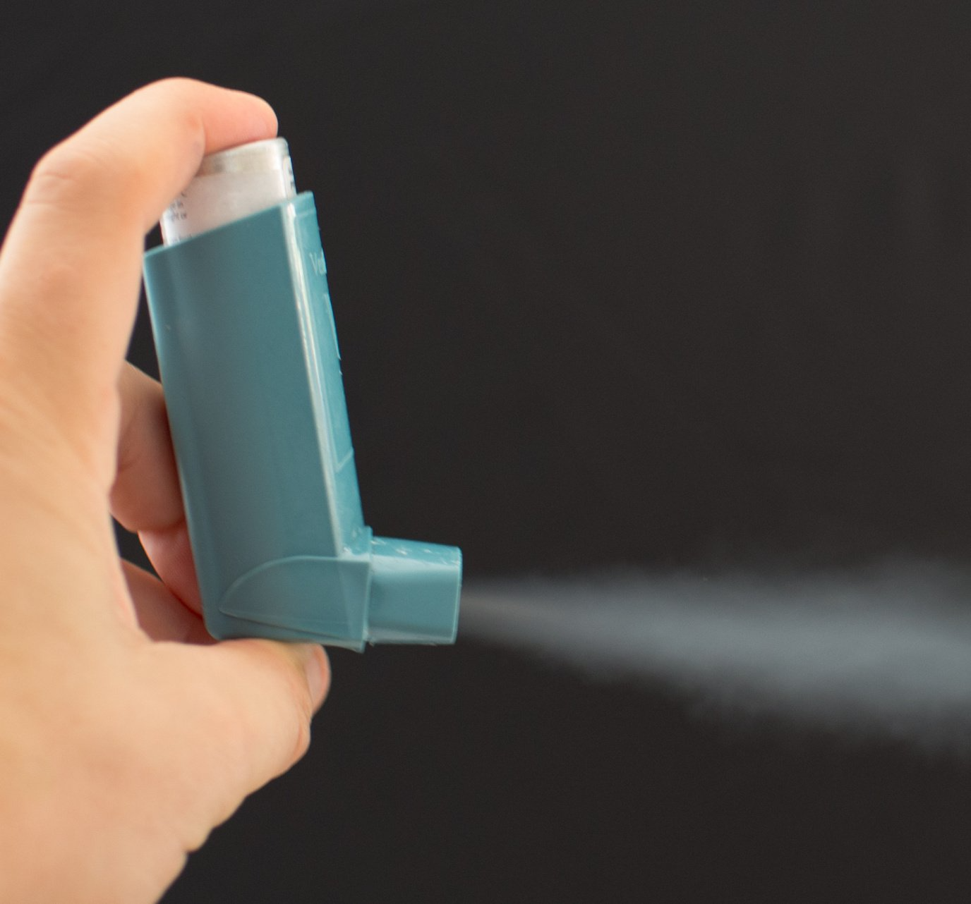 Hand holding an asthma inhaler with spray coming out of the inhaler