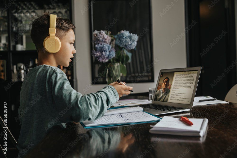Young girl learning online with headphones on her ears talking to a tutor on her laptop