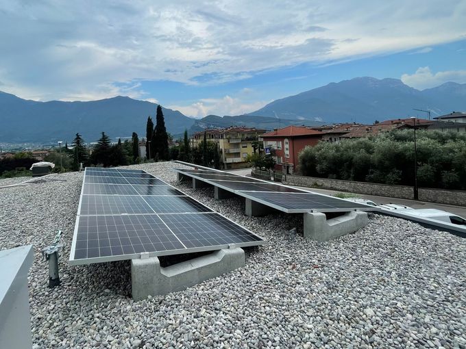 Pannelli solari installati su un tetto piano di ghiaia, con montagne e case sullo sfondo.