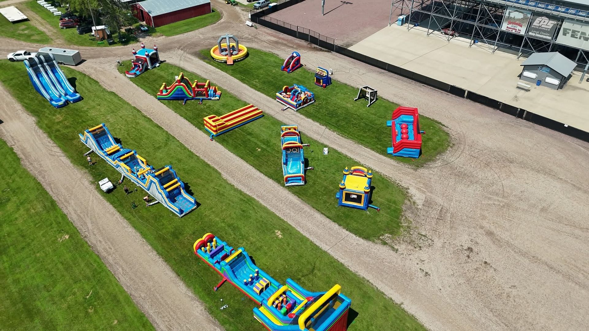 An aerial view of multiple colorful inflatable bounce houses and slides set up on a grassy field.