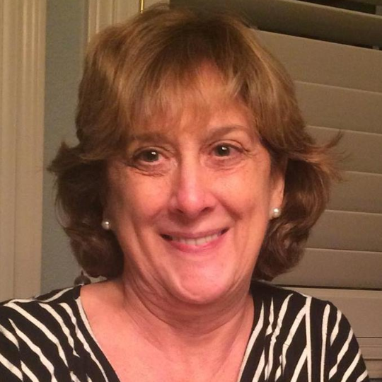 Smiling woman in a black-and-white striped top indoors, with short light brown hair.