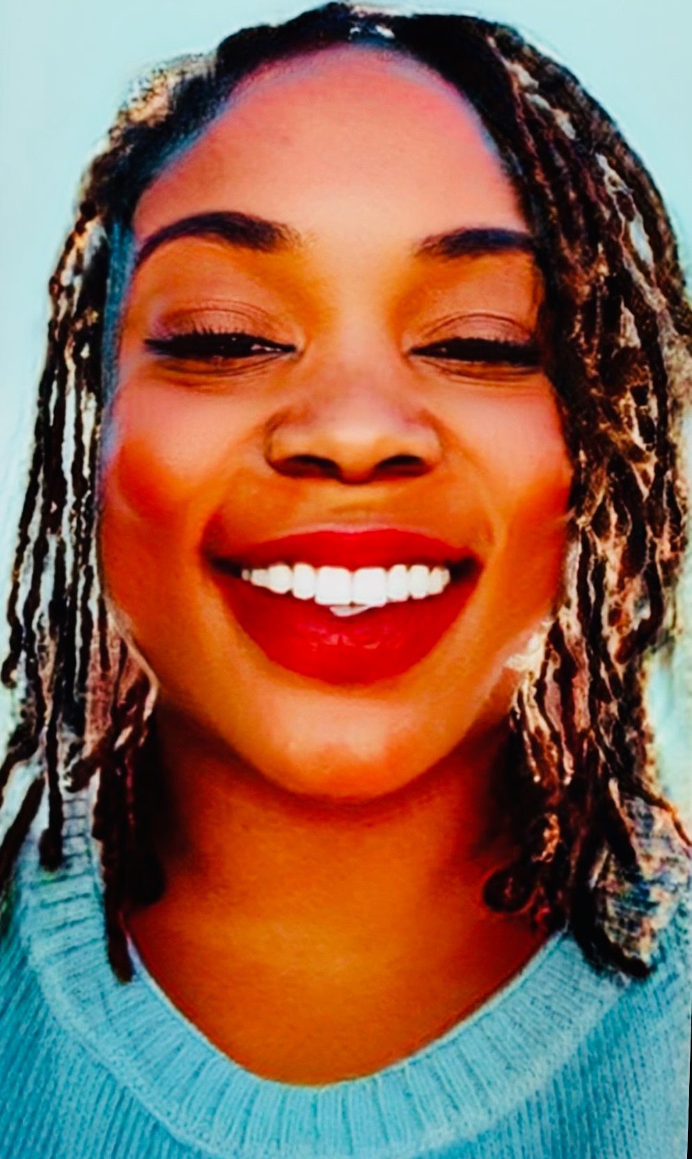 Close-up of a smiling person with braided hair wearing a light blue sweater