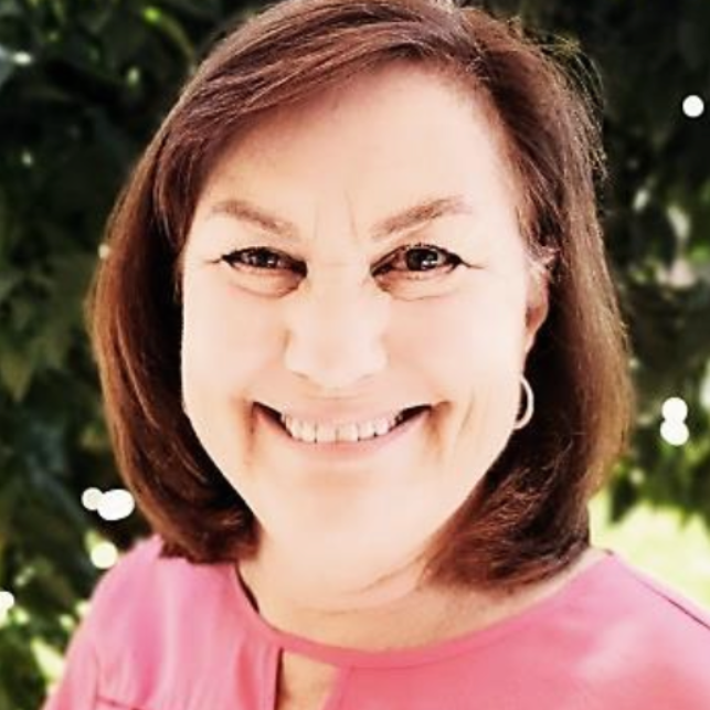 Smiling woman in a pink top outdoors with blurred greenery in the background