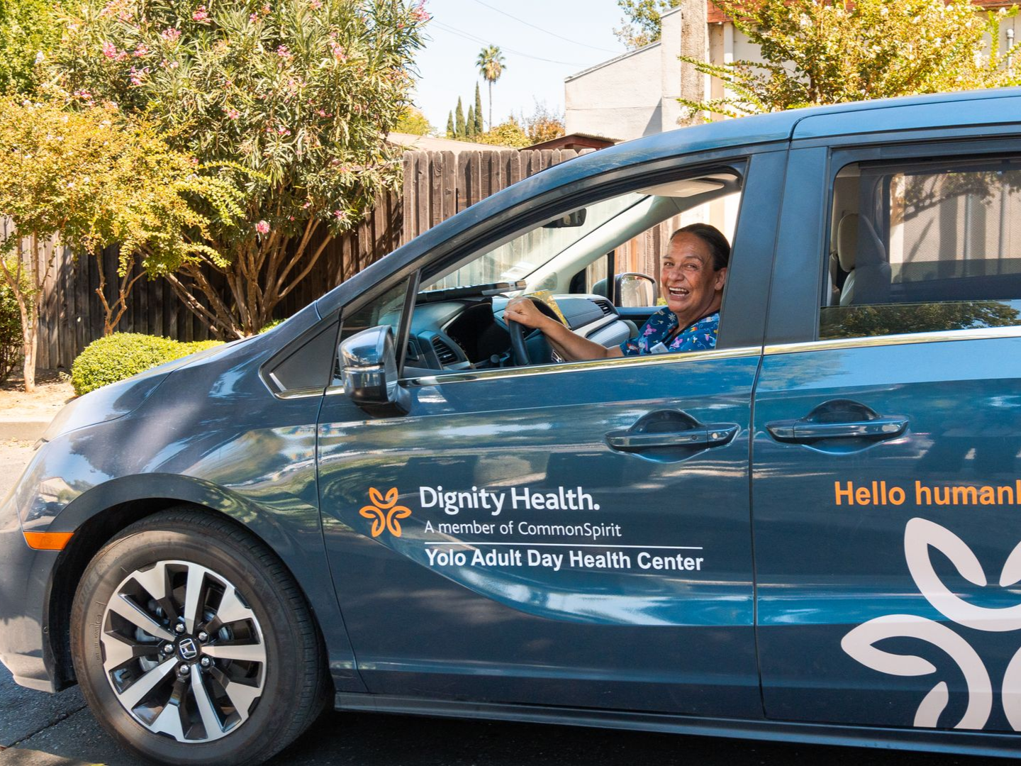 Driver smiling in a blue Dignity Health van with “Hello human” branding, parked outdoors
