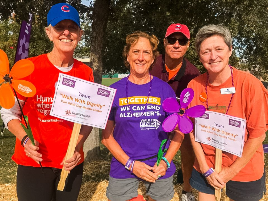 Four people in orange and purple shirts holding signs and a purple pinwheel outdoors.
