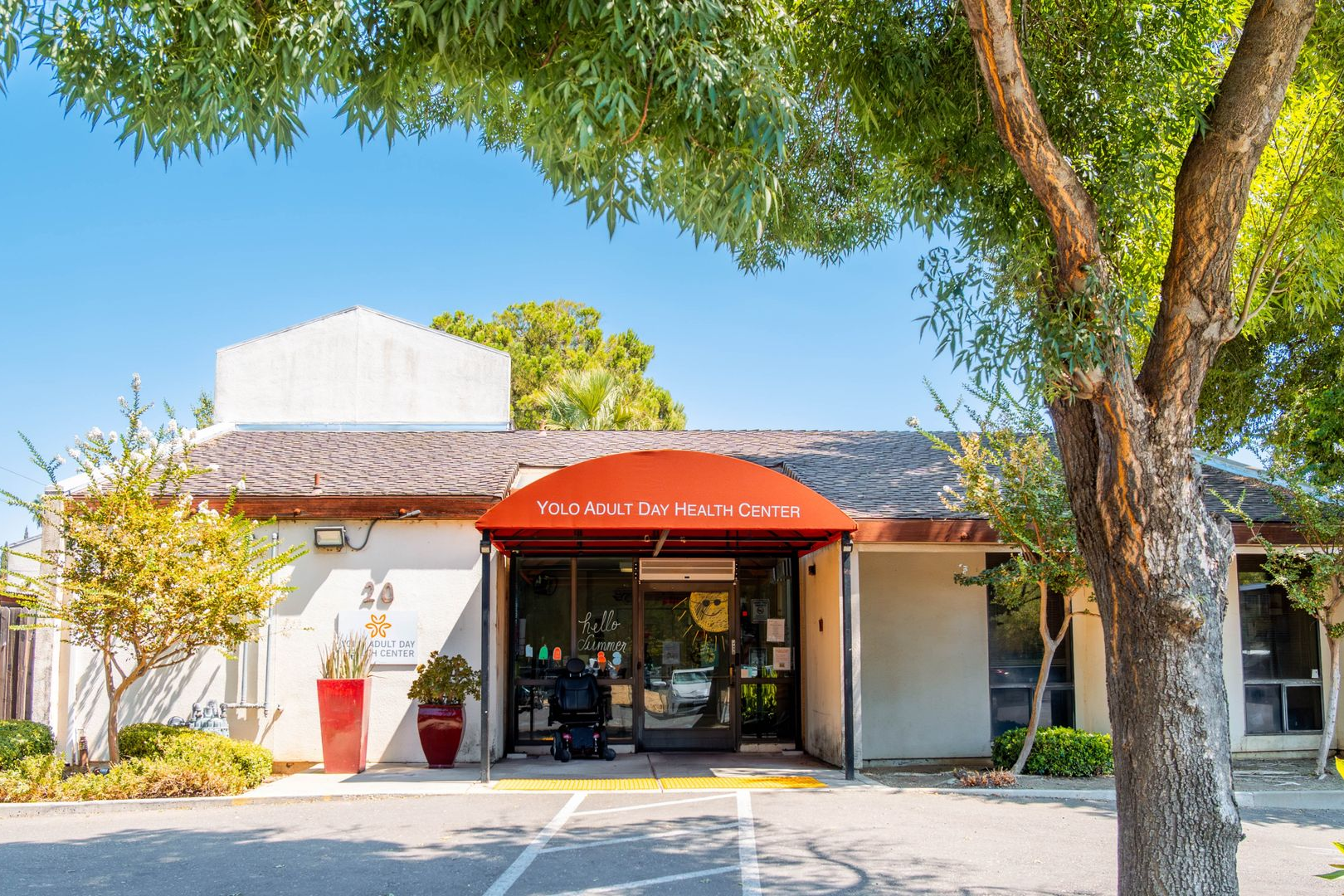 Building entrance with red awning, glass doors, and trees in front under a clear blue sky