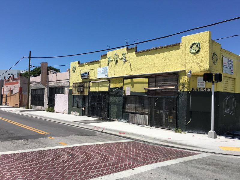 A yellow building is sitting on the corner of a street in a poor neighbourhood in miami